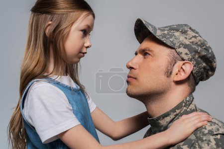 Trauriges Mädchen sieht Soldat in Militäruniform weinend während Gedenktag isoliert auf grau 