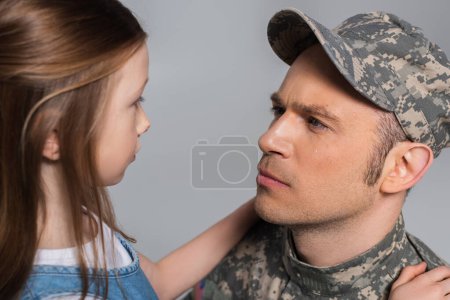 Mädchen sieht traurigen Soldaten in Militäruniform beim Gedenktag weinend zu, isoliert auf grau 