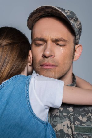 Sentimentaler Soldat in Militäruniform weint und umarmt Tochter am Gedenktag isoliert auf grau 