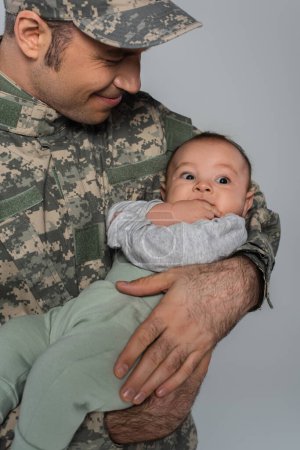 happy soldier in military uniform and cap holding newborn son isolated on grey 