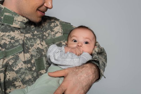 glücklicher Soldat in Uniform hält kleinen Jungen in den Armen isoliert auf grau 