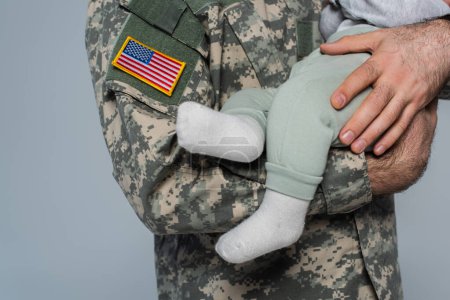 Ausgeschnittene Ansicht eines US-Soldaten in Uniform, der seinen neugeborenen Sohn isoliert auf grau hält 