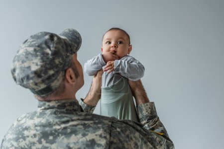 army soldier in military uniform and cap holding baby son in arms isolated on grey