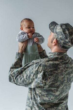 Soldat de l'armée en uniforme militaire avec casquette tenant un enfant en bas âge dans les bras isolé sur gris