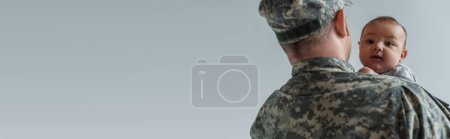 newborn boy in arms of serviceman in military uniform isolated on grey, banner 