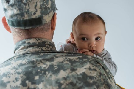 father in military uniform and cap hugging newborn son isolated on grey 