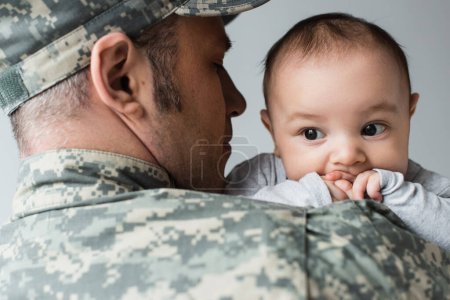 Foto de Hombre en uniforme militar y gorra abrazando hijo recién nacido aislado en gris - Imagen libre de derechos