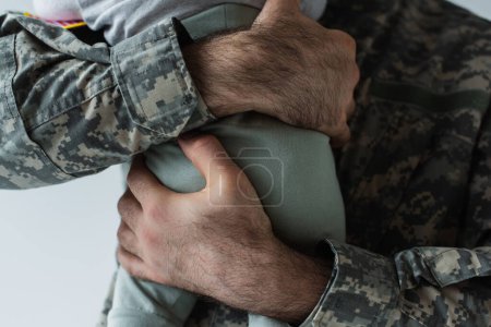 abgeschnittene Ansicht eines Soldaten in Militäruniform, der seinen kleinen Sohn isoliert auf Grau umarmt 