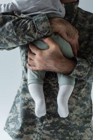 abgeschnittene Ansicht eines Vaters in Militäruniform, der seinen kleinen Sohn isoliert auf Grau umarmt 