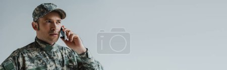 Foto de Militar con gorra y uniforme del ejército tener conversación en el teléfono inteligente aislado en gris, bandera - Imagen libre de derechos