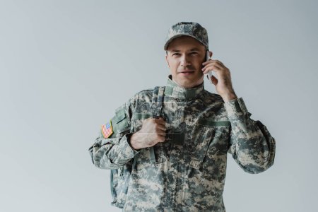 Téléchargez les photos : Joyeux militaire en uniforme de l'armée parlant sur smartphone isolé sur gris - en image libre de droit