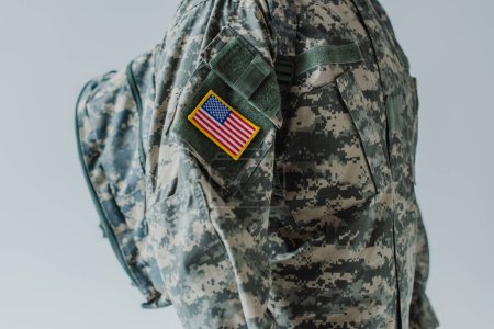 Foto de Vista recortada del militar estadounidense en uniforme del ejército de pie con mochila aislada en gris - Imagen libre de derechos