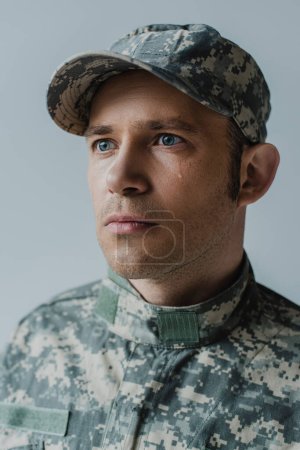 triste soldado en uniforme militar llorando durante el día conmemorativo aislado en gris 