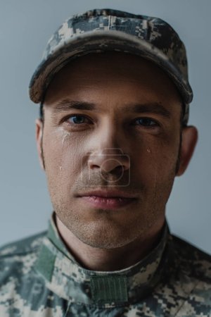 Porträt eines traurigen Soldaten in Militäruniform, der am Gedenktag weint, isoliert auf grau 