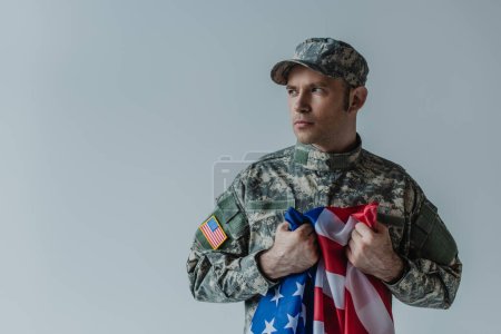 Amerikanischer Soldat hält Flagge der Vereinigten Staaten, während er am Gedenktag weint, isoliert auf grau 