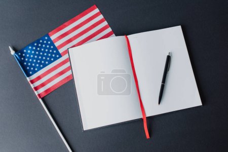 Ansicht der amerikanischen Flagge mit Sternen und Streifen in der Nähe eines leeren Notizbuchs isoliert auf schwarz 