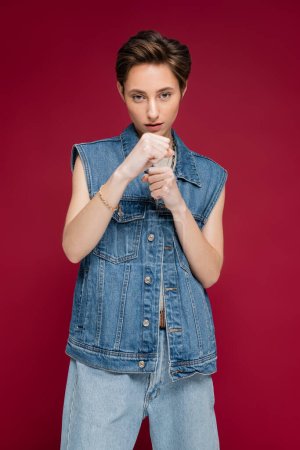 Photo for Young woman with short hair standing with clenched fists while fighting on dark red background - Royalty Free Image