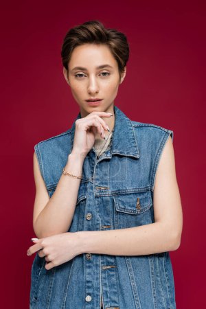 Photo for Young model with short hair posing in denim vest on dark red background - Royalty Free Image