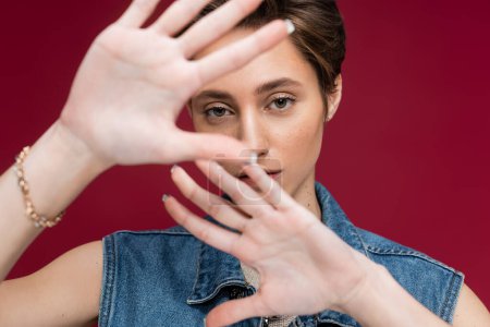young model with short hair looking at camera while gesturing on maroon background