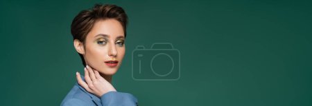 pretty young woman with short hair posing in blue blazer on turquoise green background, banner 
