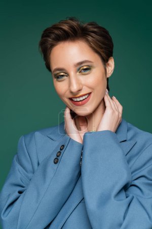 smiling young woman with short hair posing in blue suit on turquoise green background 