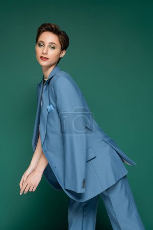 young woman with short hair posing in blue pantsuit on turquoise background 