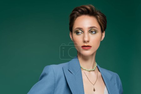 elegante junge Frau mit kurzen Haaren und hellem Make-up schaut vereinzelt auf Türkis weg 