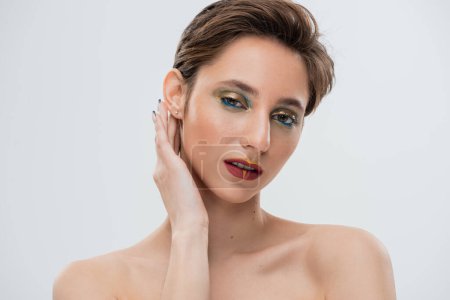 Porträt eines jungen Models mit hellem Make-up, das Hemdhaare fixiert und in die Kamera schaut, isoliert auf grau 