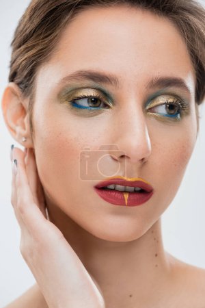 Nahaufnahme der jungen Frau mit hellen Augen Make-up Fixierung Hemdhaar und Blick weg isoliert auf grau 