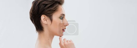 Téléchargez les photos : Profil de jeune femme au maquillage éclatant touchant menton isolé sur gris, bannière - en image libre de droit
