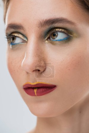 close up of young woman with shiny eye makeup and red lips isolated on grey
