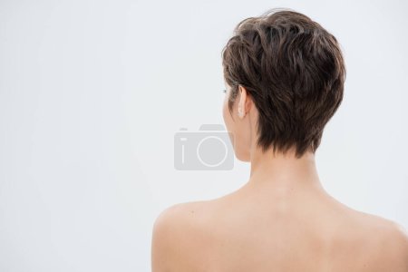 back view of young woman with short hair and bare shoulders isolated on grey 