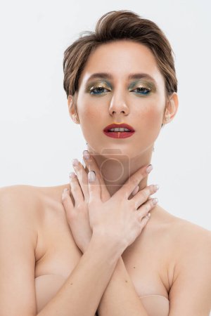 Charmante junge Frau mit glänzenden Augen Make-up posiert in trägerlosen BH isoliert auf grau 