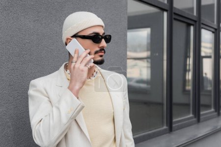 Foto de Hombre homosexual de moda en gafas de sol hablando por teléfono móvil en la calle urbana - Imagen libre de derechos