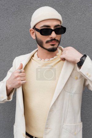 modny gej człowiek w kurtka i okulary stojąc na zewnątrz 