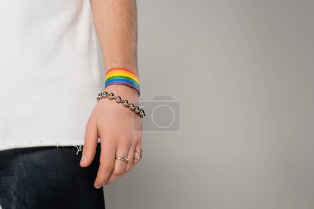 Vista recortada del hombre homosexual con lgbt pulsera en la mano de pie aislado en gris  