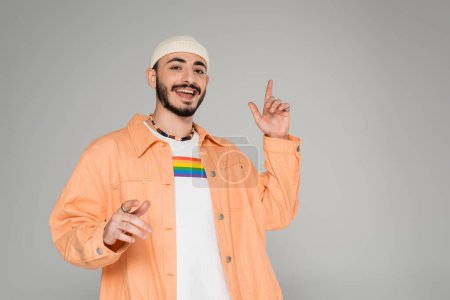 Stylish gay man with lgbt flag on t-shirt pointing with fingers isolated on grey  