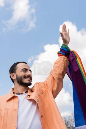alegre gay hombre con lgbt bandera ondeando mano en urbano calle internacional día contra homofobia