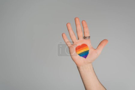 Téléchargez les photos : Cropped view of gay man with lgbt flag in heart shape on hand isolated on grey, Journée internationale contre l'homophobie - en image libre de droit