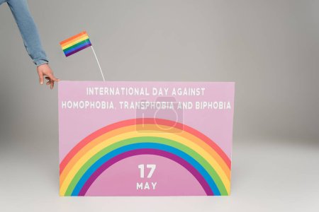 Vista recortada del hombre gay cerca de la pancarta con el Día Internacional contra la Homofobia, Transfobia y Bifobia escrito en gris 