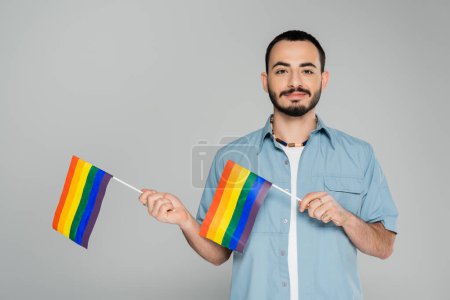 Retrato de un hombre gay barbudo sosteniendo banderas lgbt aisladas en gris, Día Internacional contra la Homofobia 