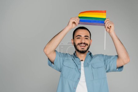 Hombre homosexual positivo sosteniendo bandera lgbt aislada en gris con espacio para copias, Día Internacional contra la Homofobia 