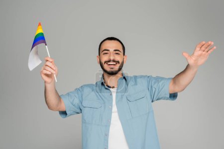 Hombre homosexual positivo y barbudo con bandera lgbt aislada el día gris de la homofobia internacional