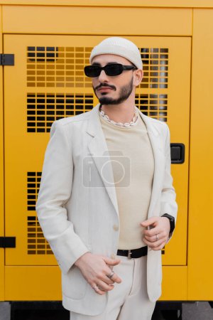 Photo for Fashionable homosexual man in hat and sunglasses standing on urban street - Royalty Free Image