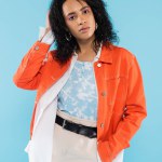 brunette african american woman in trendy jacket posing with hand in pocket of cotton shorts isolated on blue
