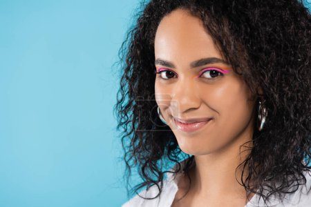 Téléchargez les photos : Portrait de femme brune afro-américaine avec maquillage et peau parfaite regardant la caméra isolée sur bleu - en image libre de droit