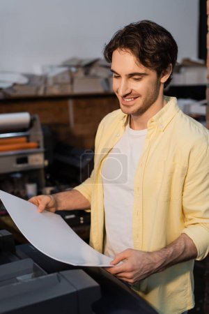 fröhlicher Verleger hält leeres Papier in der Hand und lächelt im Druckzentrum 
