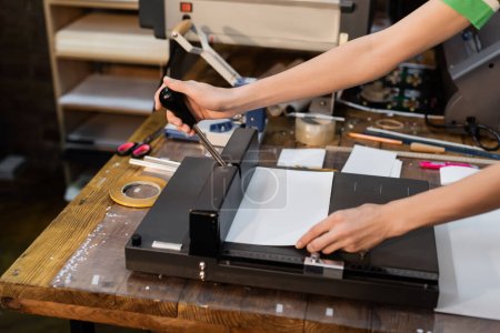 Foto de Recortado vista de la mujer de corte de papel durante el uso de trimmer en el centro de impresión - Imagen libre de derechos