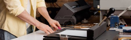 vista recortada del tipógrafo cortando papel con cuchillo cerca del recortador de papel en el centro de impresión, pancarta 