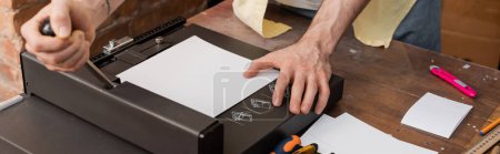 vista recortada del hombre tatuado utilizando la máquina cortadora de papel en el centro de impresión moderno, pancarta 